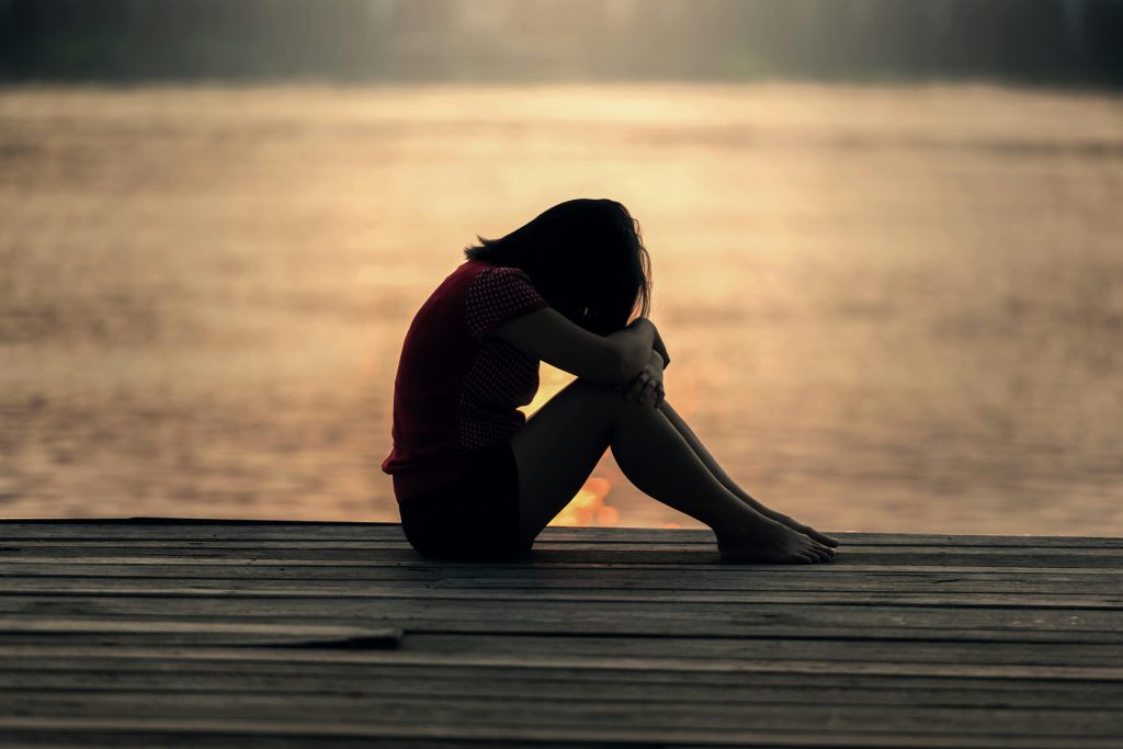 Une femme assise seule sur un ponton en bois au bord d'un lac, montrant la solitude et la réflexion.