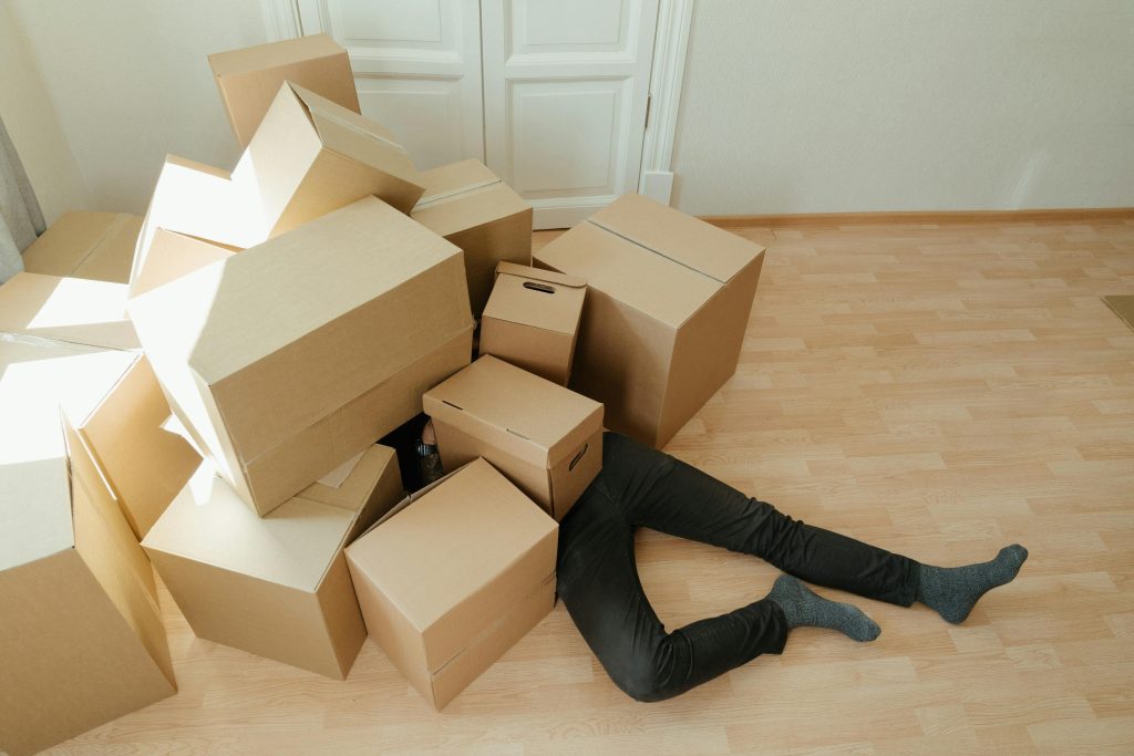 A person overwhelmed by cardboard boxes during a home move, symbolizing stress and relocation. Une personne submergée par des cartons lors d'un déménagement, symbolisant le stress et le changement de domicile.
